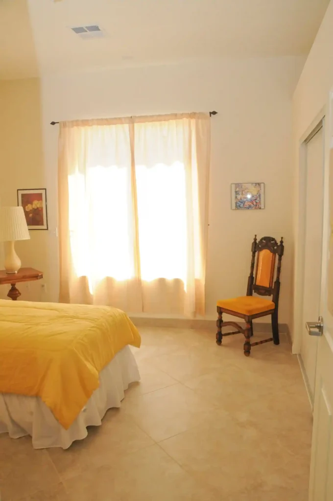 Inner view of a bedroom of Nevada Memory Care in which you can see a chair and a half portion of a bed and a wall with a curtain on it.